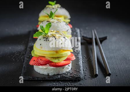 Aromatischer und süßer Sushi-Burger mit Erdbeeren und Mascarpone auf dunklem Teller. Japanisches Dessert aus Reis und Früchten. Stockfoto