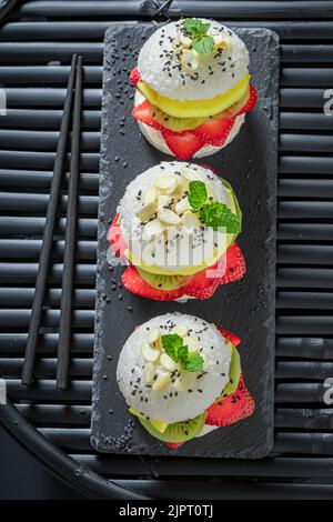 Aromatischer und süßer Sushi-Burger mit tropischen Früchten auf dunklem Teller. Japanisches Dessert aus Reis und Früchten. Stockfoto
