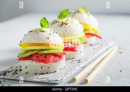 Aromatischer und süßer Sushi-Burger mit Erdbeeren und Mango auf weißem Teller. Japanisches Dessert aus Reis und Früchten. Stockfoto