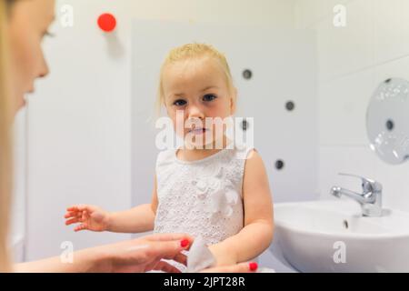 Die Lehrerin hilft einem niedlichen kleinen Mädchen, sich im Kindergarten die Hände zu waschen. Hochwertige Fotos Stockfoto