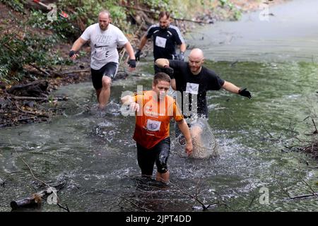 Genthin, Deutschland. 20. August 2022. Teilnehmer der '6. Genthiner Matsch-Wolke' joggen durch einen alten Bach. 270 Teilnehmer kämpfen sich durch Staub, Schlamm, Kletterwände und über zwanzig weitere Hindernisse. In diesem Jahr führt der 12 Kilometer lange Hindernisparcours auch durch Schloss Parchen. Quelle: Peter Gercke/dpa-Zentralbild/dpa/Alamy Live News Stockfoto