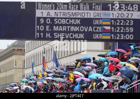 München, Deutschland. 20. August 2022. Leichtathletik: Europameisterschaften, 20 Kilometer Gehweg, Finale, Frauen, Zuschauer beobachten das Rennen unter Sonnenschirmen auf einer Tribüne am Odeonsplatz. Quelle: Soeren Stache/dpa/Alamy Live News Stockfoto