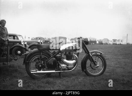 1950s, historisch, draußen auf einem Feld auf einem Caravanplatz, eine Dame, die neben einigen Autos steht und ein britisch hergestelltes BSA-Motorrad der Zeit auf dem Gras abstellt, England, Großbritannien. Gegründet 1861 als Birmingham Small Arms Company Ltd, für die Herstellung von Schusswaffen, wurde 1903 eine Motorradsparte der BSA gegründet und das erste Motorrad, das 1910 auf den Markt kam. Im Jahr 1950s war BSA Motorcycles der größte Motorradhersteller der Welt. Stockfoto