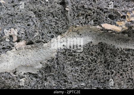 Eine Nahaufnahme eines Gelenks zwischen zwei riesigen Lavagesteinen, die in einer schwarz-weißen Monochrom-Wand stehen. Stockfoto