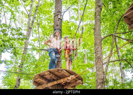Mutter und Sohn klettern in extreme Straße Trolley Zipline im Wald auf Karabiner Sicherheitslink auf Baum zu Baum top Seil Abenteuerpark. Familienwochenende Stockfoto