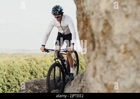 Ausgerüsteter Profi-Radler mit Mountainbike auf dem Trail im felsigen Gelände, Erwachsener, der seinen extremen Hobby-Stand mit Fahrrad genießt Stockfoto