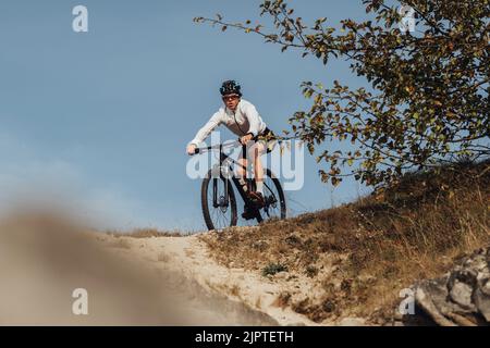 Ausgerüsteter Profi-Radler fährt mit seinem Mountainbike eine Piste hinunter, der Sportler fährt mit dem Fahrrad vom Berg herunter Stockfoto