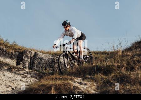 Ausgerüsteter Profi-Radler fährt mit seinem Mountainbike eine Piste hinunter, der Sportler fährt mit dem Fahrrad vom Berg herunter Stockfoto