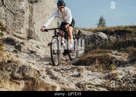 Ausgerüsteter Profi-Radler fährt mit seinem Mountainbike eine Piste hinunter, der Sportler fährt mit dem Fahrrad vom Berg herunter Stockfoto