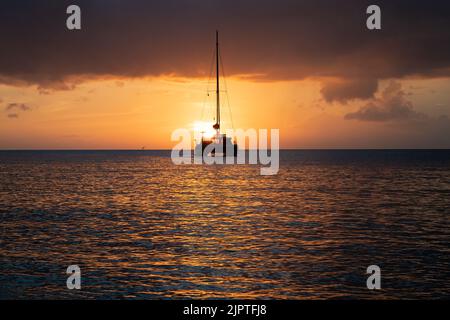 Segelboot, das in die untergehende Sonne am Meereshorizont segelt Stockfoto