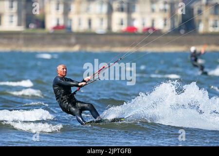 Troon, Großbritannien. 20. August 2022. Starke südwestliche Flügel lockten eine Reihe von Kitesurfern in die Bucht vor dem Strand von Troon. Die teilweise bis zu 25mph stürzenden Winde am Firth of Clyde boten ideale Bedingungen für den Sport. Kredit: Findlay/Alamy Live Nachrichten Stockfoto