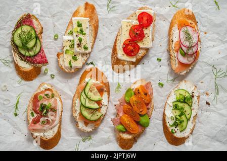 Verschiedene kleine Sandwiches mit Frischkäse, Gemüse und Salami. Stockfoto