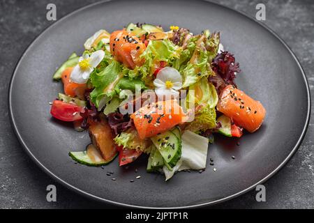 Salat mit Lachs, frischem Gemüse, Tomaten und Gurken sowie Salatblättern Stockfoto