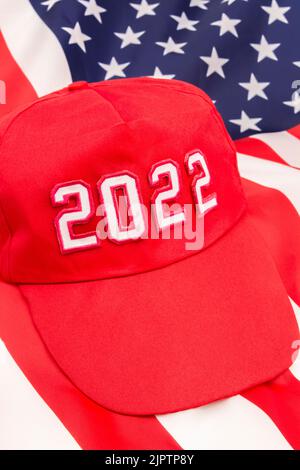 Red MAGA-Typ Hut mit 2022 auf Hintergrund US Stars and Stripes Flagge. Für republikanische Siege bei den Midterm-Wahlen in den USA im November 2022 und der republikanischen Roten Welle. Stockfoto