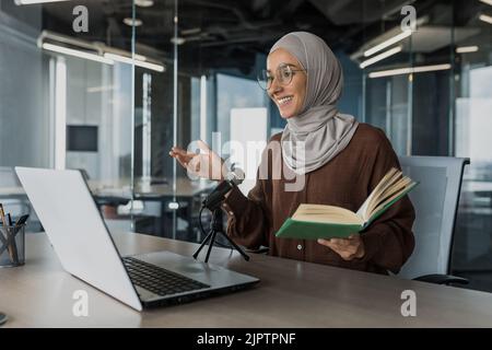 Junge schöne muslimische Frau in Hijab arbeiten in modernen Büro mit professionellen Mikrofon, um Audio-Podcast Lesung religiöse Buch Online-Radio aufnehmen Stockfoto