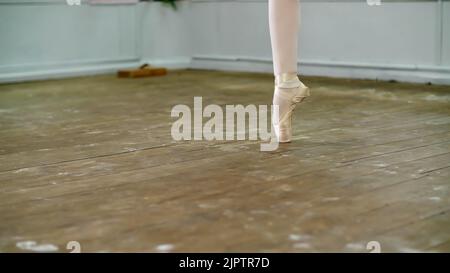 Nahaufnahme, in der Tanzhalle, Ballerina Schritt pointe durchführen, steht sie auf Zehen in spitzenschuhen elegant, auf einem alten Holzboden, in der Ballettklasse. Hochwertige Fotos Stockfoto