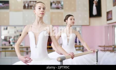 Im Ballettsaal werden zwei Mädchen in weißem Balletttutu, beim Ballett verlobt, Proben drehen, Junge Ballerinas stehen am Geländer im Ballettsaal. Hochwertige Fotos Stockfoto