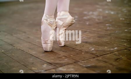 Nahaufnahme, in der Tanzhalle, Ballerina Schritt pointe durchführen, steht sie auf Zehen in spitzenschuhen elegant, auf einem alten Holzboden, in der Ballettklasse. Hochwertige Fotos Stockfoto