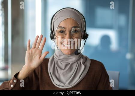 Nahaufnahme Porträt von jungen schönen muslimischen Geschäftsfrau, Tech-Support-Mitarbeiter in Hijab und Brille, Kundendienstmitarbeiter lächelnd und Blick auf die Kamera, mit Headset, Videoanruf. Stockfoto