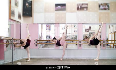 In der Tanzhalle dehnen sich junge Ballerinas in schwarzen Trikots, die in der Ballettklasse in der Nähe des Barres am Spiegel stehen. Hochwertige Fotos Stockfoto