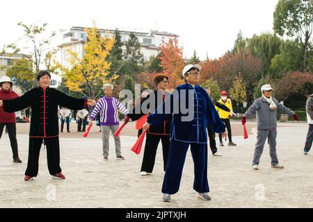 Chinesische Senioren üben Tai Chi mit Kung Fu Fans am frühen Morgen auf dem Stadtplatz von Lijiang. Stockfoto