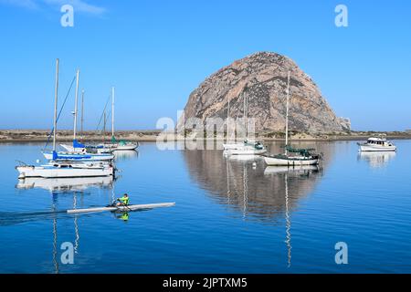 Verankerte Boote und ein Mann, der auf dem Kanu in der Nähe des Morro Rock in der Morro Bay reitet. Stockfoto