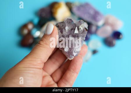 Schöne lila Amethyst Kristalle in der Hand. Druse von Amethyst in der Hand einer Frau vor dem Hintergrund anderer Edelsteine. Selektiver Fokus. Stockfoto