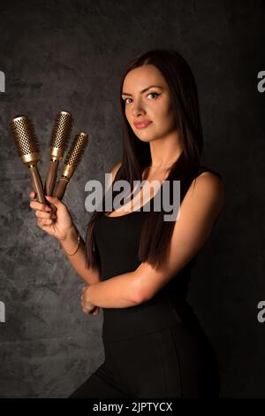 Der Friseurmeister hält Haarbürsten in der Hand. Porträt auf schwarzem Hintergrund Stockfoto