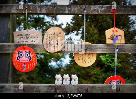 Japanische Gebetstafeln namens Ema und Katzenfiguren namens Maneki-Neko auf Japanisch (wörtlich „lockende Katze“). Mount Misen, Insel Miyajima, Japan. Stockfoto