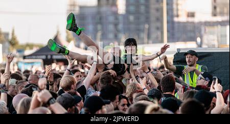 Hamburg, Deutschland. 20. August 2022. Besucher des Metal- und Rock-Festivals 'Elbriot' 2022 bewegen eine junge Frau auf ihren Händen während des Crowdsurfens auf die Bühne. Quelle: Markus Scholz/dpa/Alamy Live News Stockfoto