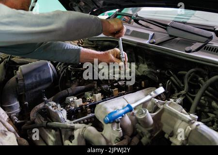 Hände des kaukasischen Mechanikers, der Teile des Dieselmotors eines modernen SUV abschraubt Stockfoto
