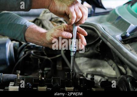 Hände des kaukasischen Mechanikers, der Teile des Dieselmotors eines modernen SUV abschraubt Stockfoto