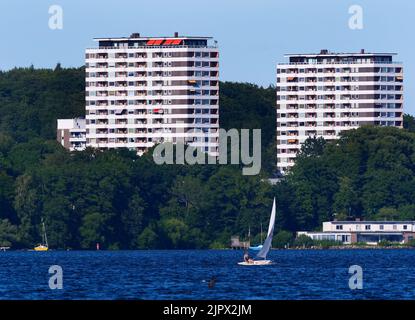 09. August 2022, Schleswig-Holstein, Plön: 09.08.2022, Ploen. In Ploen stehen zwei Hochhäuser. Vor ihnen ist der große Ploen See zu sehen, auf dem ein Seemann mit seinem Beiboot segelt. (Aufnahme mit einem starken Teleobjektiv). Foto: Wolfram Steinberg/dpa Foto: Wolfram Steinberg/dpa Stockfoto