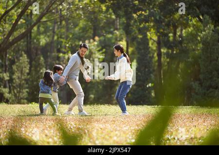 Junge asiatische Familie mit zwei Kindern, die Spaß beim Spielen im Park haben Stockfoto