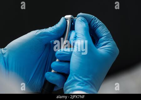 Ein Foto aus der Nähe einer Hand eines Zahnarztes, der eine zahnärztliche Hochgeschwindigkeits-Turbine in das Edelstahlhandstück der Turbine hält. Stockfoto