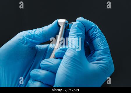 Ein Foto aus der Nähe einer Hand eines Zahnarztes, der eine zahnärztliche Hochgeschwindigkeits-Turbine in das Edelstahlhandstück der Turbine hält. Stockfoto