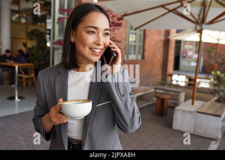 Lächelnde asiatische professionelle Frau, die vor dem Büro auf dem Handy spricht. Stockfoto