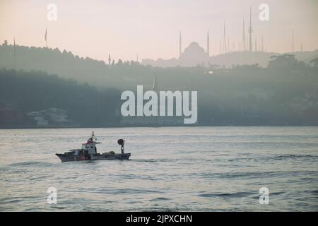 Türkischer Fischer, der im Boot im Meer segelt. Blick vom Bosporus auf das Militärgymnasium Kuleli und die Camlica-Moschee. Stockfoto