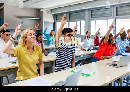 Gymnasiasten heben die Hand, um während der Vorlesung im Klassenzimmer eine Frage zu stellen Stockfoto