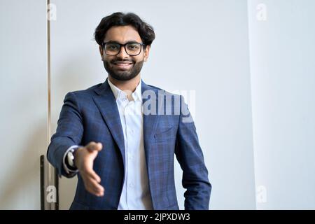 Lächelnder junger indischer Geschäftsmann, der Anzug mit ausgestreckter Hand zum Händeschütteln trägt. Stockfoto