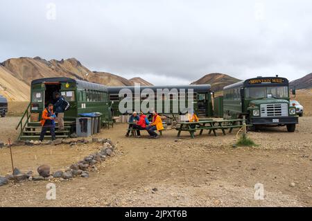 Menschen, die auf Bänken sitzen und in der Nähe von Green US Schulbussen in einer Bergkette in Island essen Stockfoto