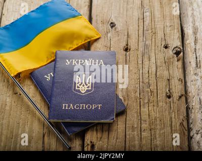 Ukrainische gelb-blaue Flagge und zwei biometrische ukrainische Pässe auf einem hölzernen Hintergrund. Auslandsreisen, Identifikation, Patriotismus, Demokratie, Russisch Stockfoto