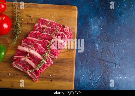 Rohe Fleischsteaks aus Rindfleisch, Schweinefleisch auf einem Holzschneidebrett auf blauem Marmorboden. Auf dem Foto befinden sich keine Personen. Es ist freier Speicherplatz zum Einfügen vorhanden Stockfoto