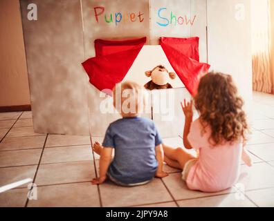 Bereit für ein magisches Puppentheater. Zwei kleine Geschwister sehen sich zu Hause ein Puppentheater an. Stockfoto