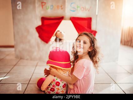 Das Puppentheater steht kurz vor dem Start. Porträt eines niedlichen kleinen Mädchens, das zu Hause ein Puppentheater ansieht. Stockfoto