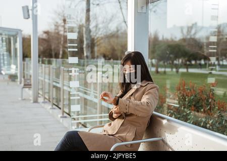 Frau, die auf einem Bahnhof sitzt und ihre Armbanduhr anschaut Stockfoto