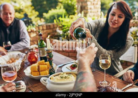 Eine Frau, die jemanden Wein an einen Esstisch gießt. Stockfoto