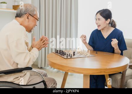 Asiatische Krankenschwester, Ärztin, die hilft, kümmern sich und spielen Schach mit Senior Asian Patient Mann, um den Geist zu entspannen Stockfoto