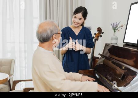 Asiatische Krankenschwester, Arzt Frau Assisting kümmern und zufrieden sein mit Senior asiatischen Patienten Mann Klavier spielen, um den Geist zu entspannen Stockfoto