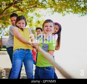 Wir mögen klein sein, aber wir sind stark. Eine vielfältige Gruppe von Kindern, die draußen am Tauziehen spielen. Stockfoto